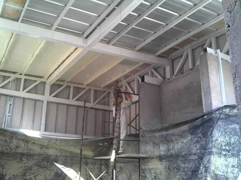Operario aplicando poliuretano en el techo de un galpón desde un andamio